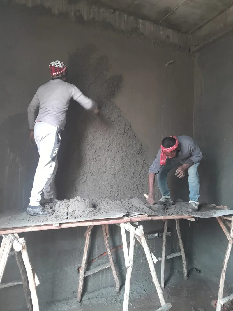 Masons applying wall plaster on scaffolding